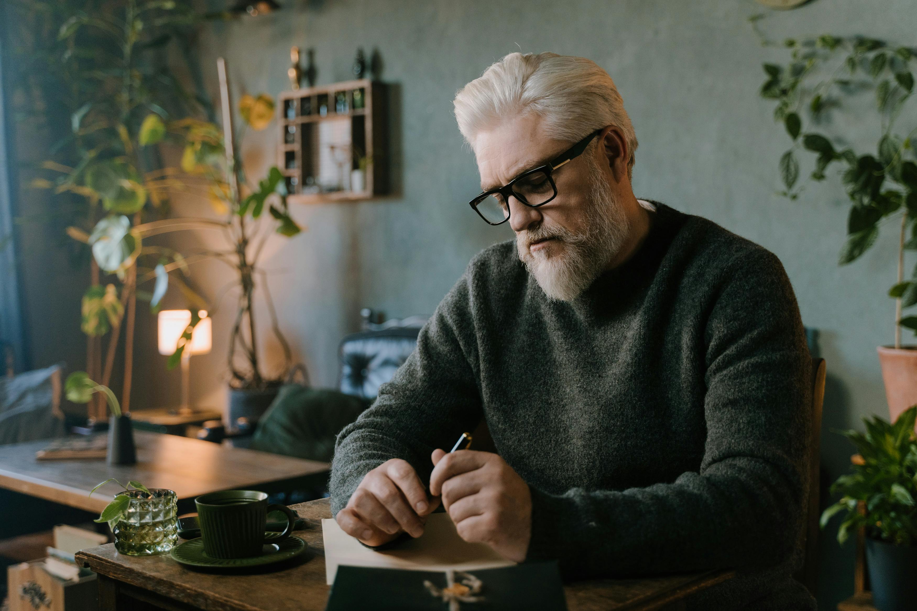 An older man seated in reflection in a softly lit room.