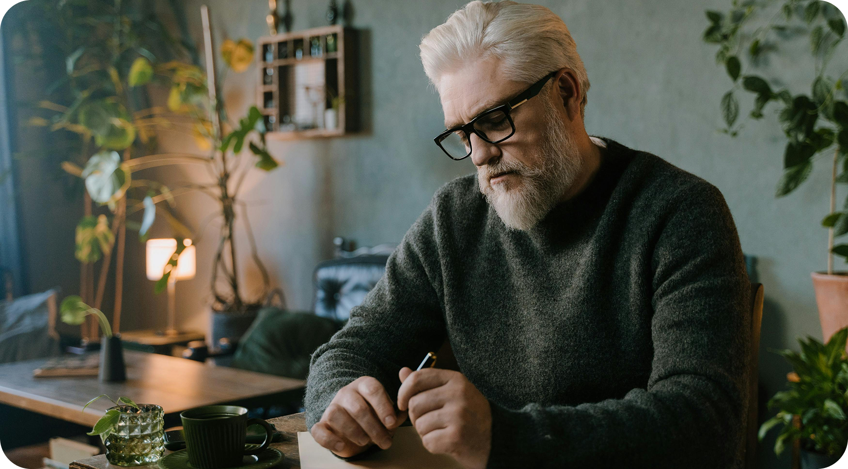 An older man seated in reflection in a softly lit room.
