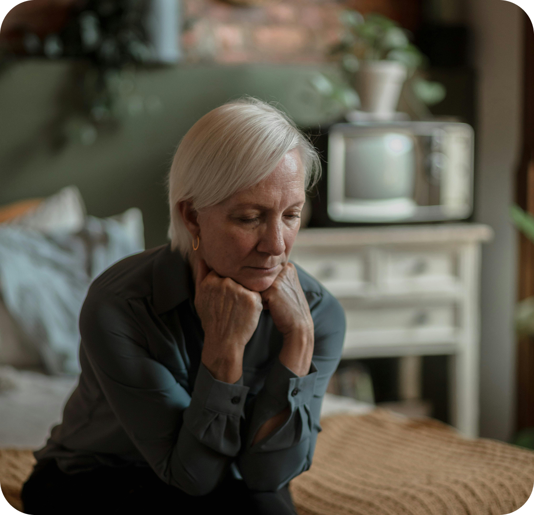 A woman sitting thoughtfully on the edge of a bed.