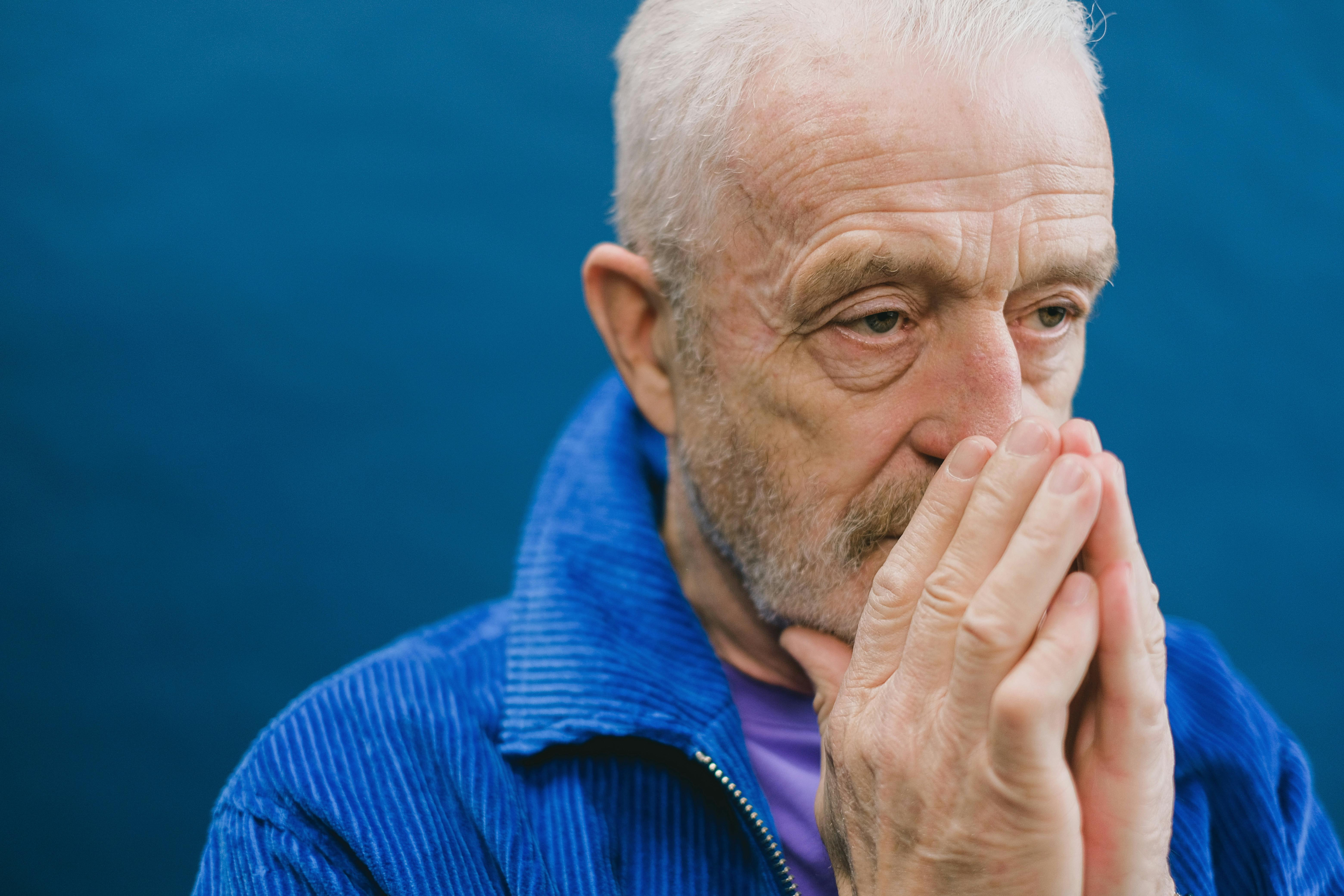 An older man in a blue jacket sitting in reflection.