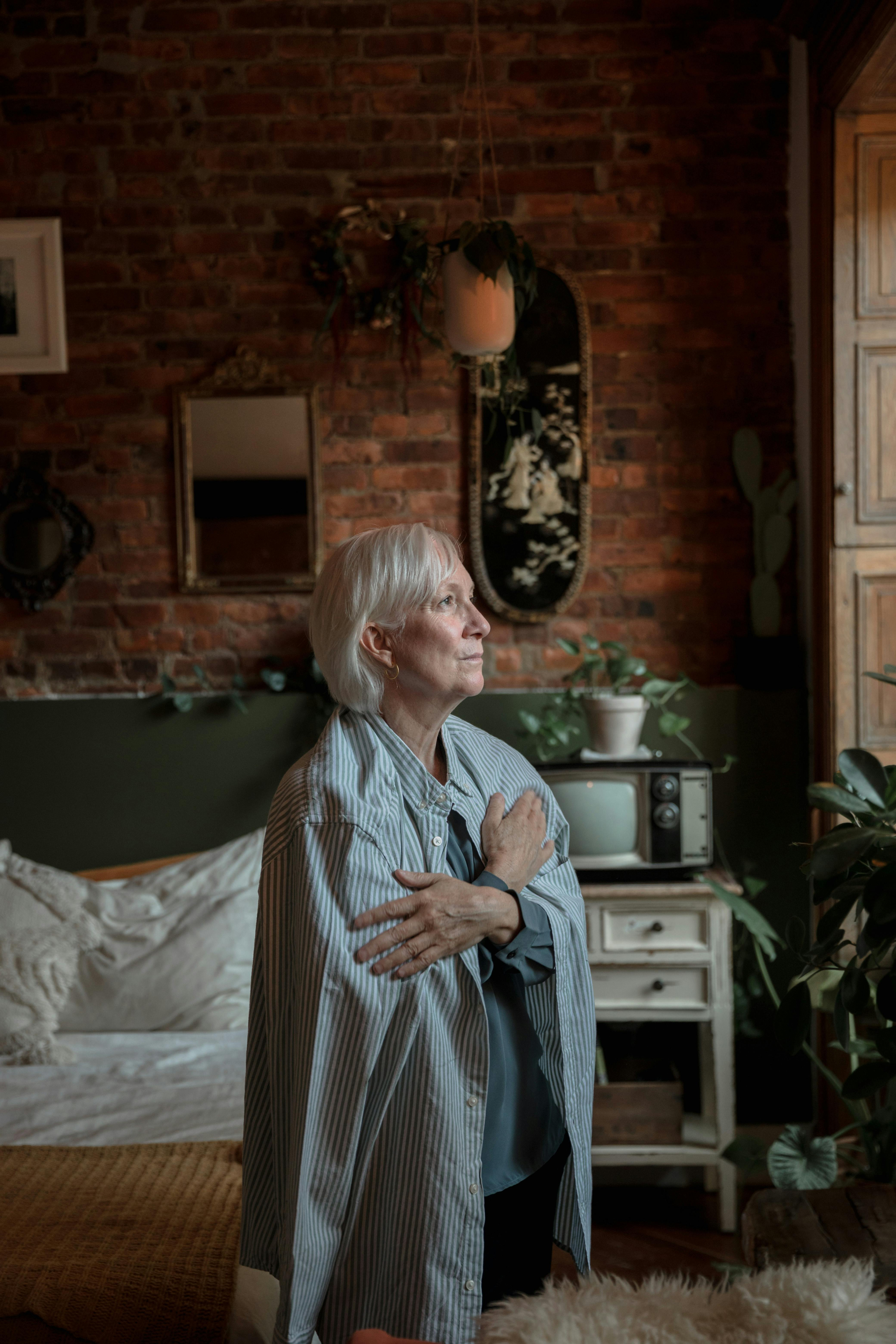 A woman sitting quietly on a bed while someone supports her in the background.