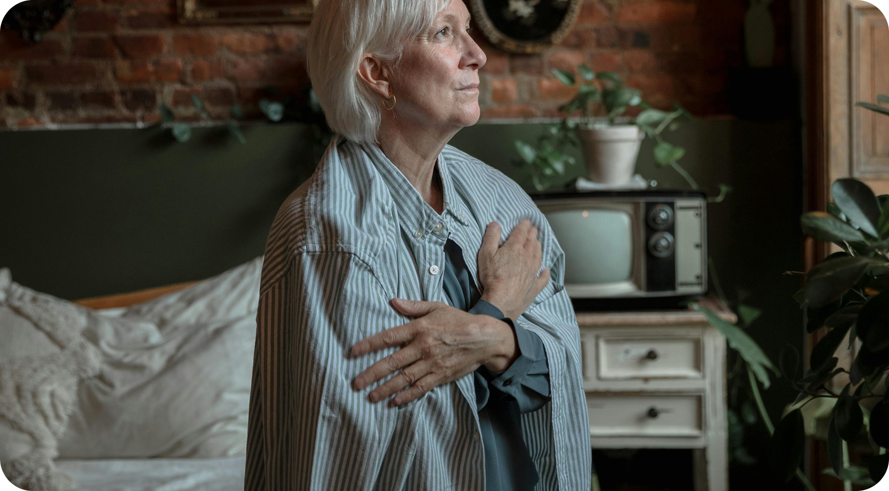 A woman sitting quietly on a bed while someone supports her in the background.